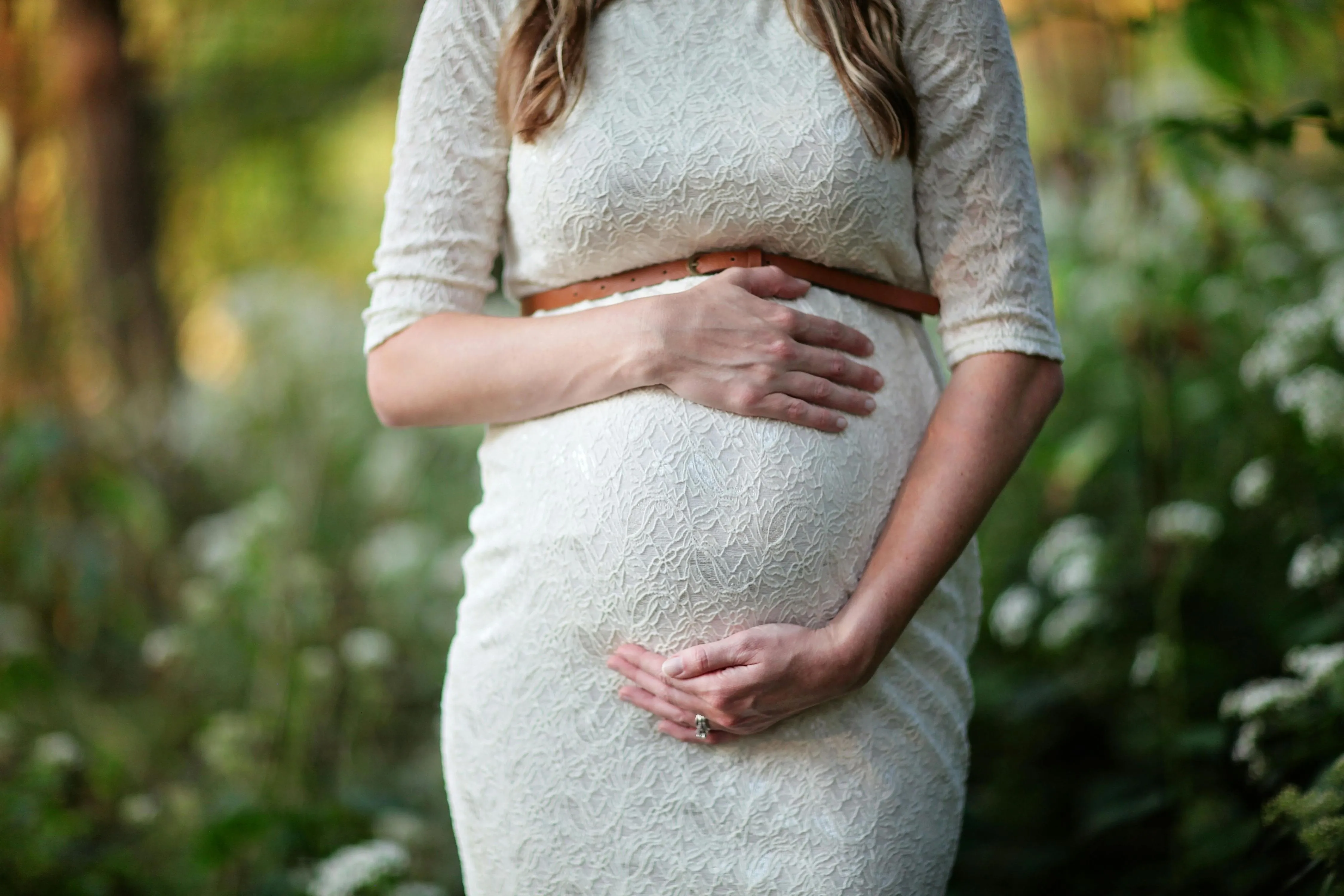 A pregnant woman in a white dress holding her belly