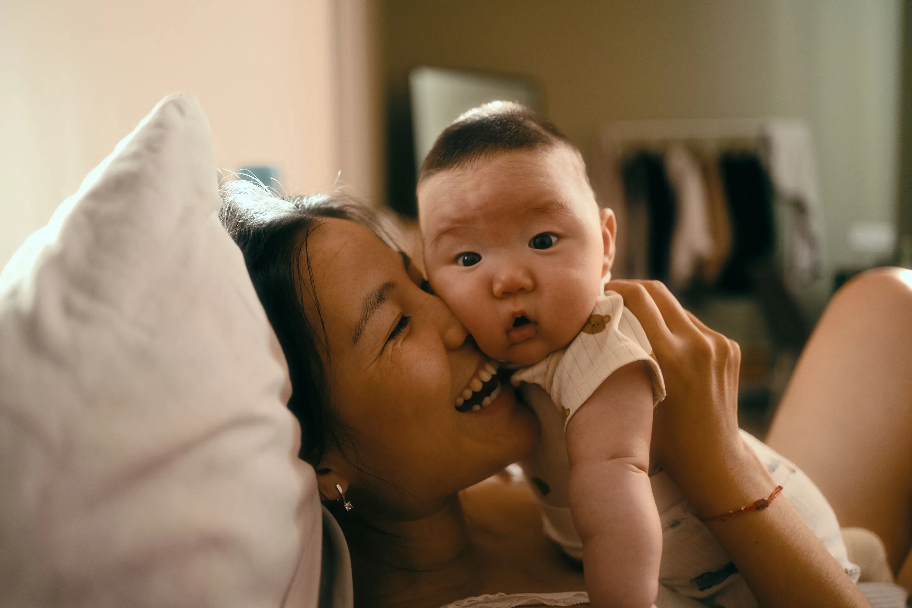 Mother smiling while snuggling baby in bed